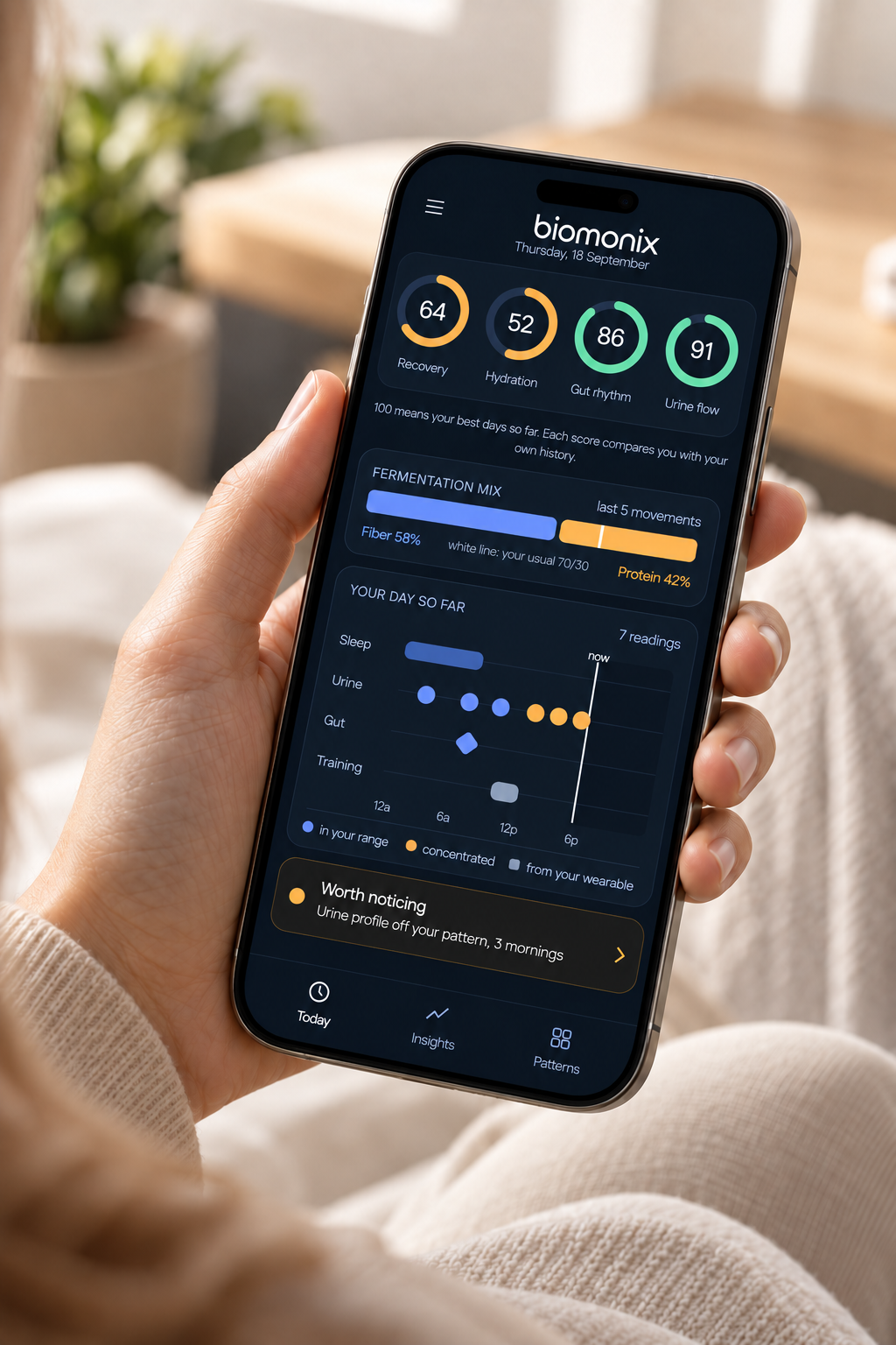 A hand holding a phone with the Biomonix app showing recovery, hydration, gut rhythm and urine flow scores